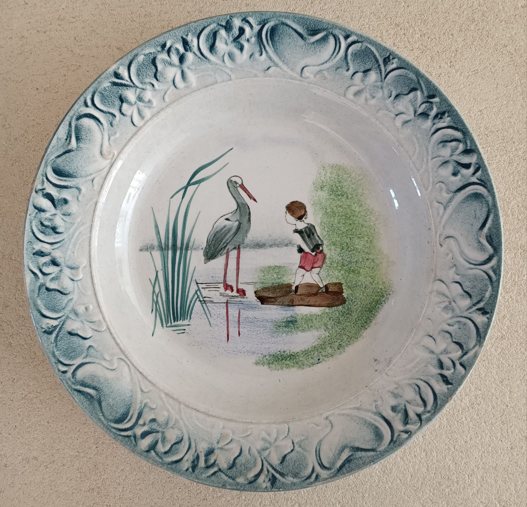 Plat de service terre de fer à décor d'enfant et cigogne