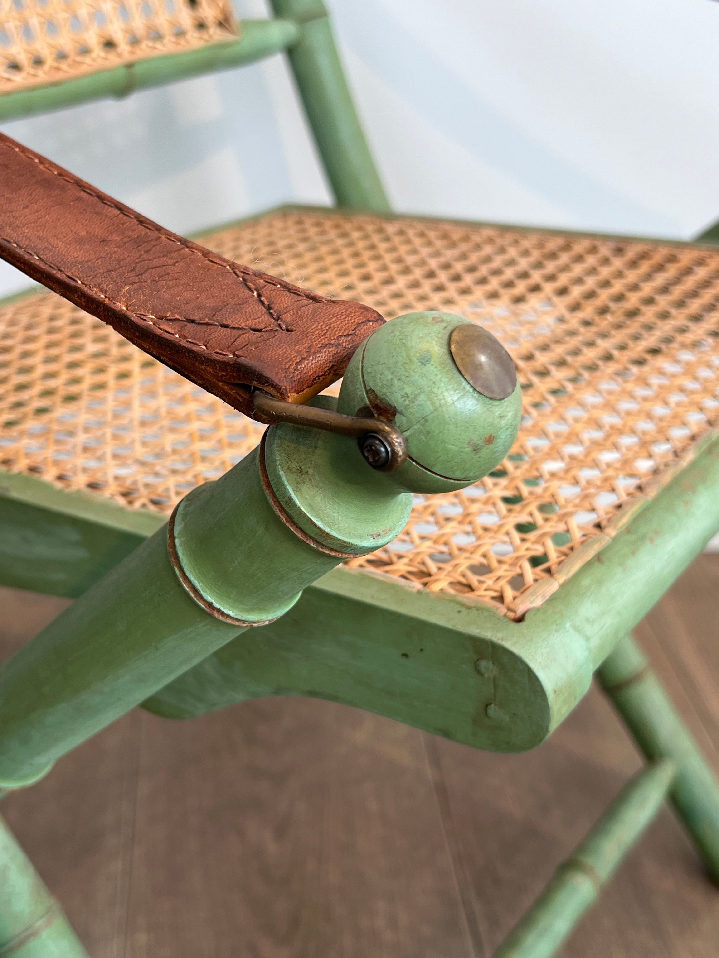 Paire de chaises safari pliantes façon faux-bambou patiné, dossiers et assises cannées et repose-bras en cuir