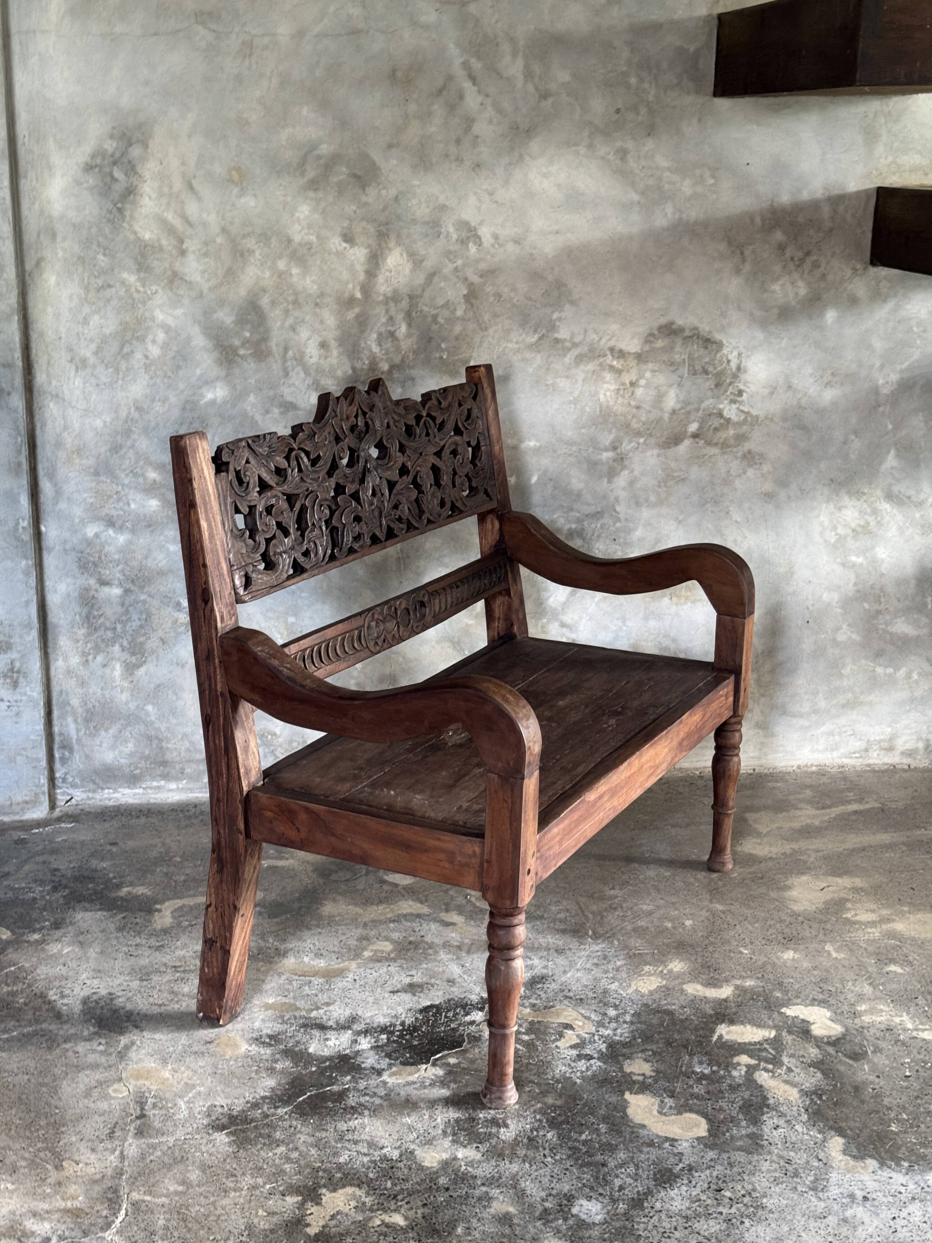 Small antique Indonesian bench in carved teak with plant and floral motifs.