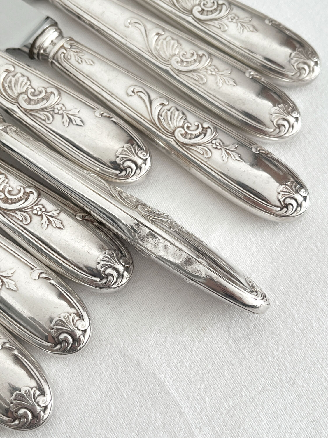 12 antique silver-plated knives with acanthus shell decoration and stainless steel blades.