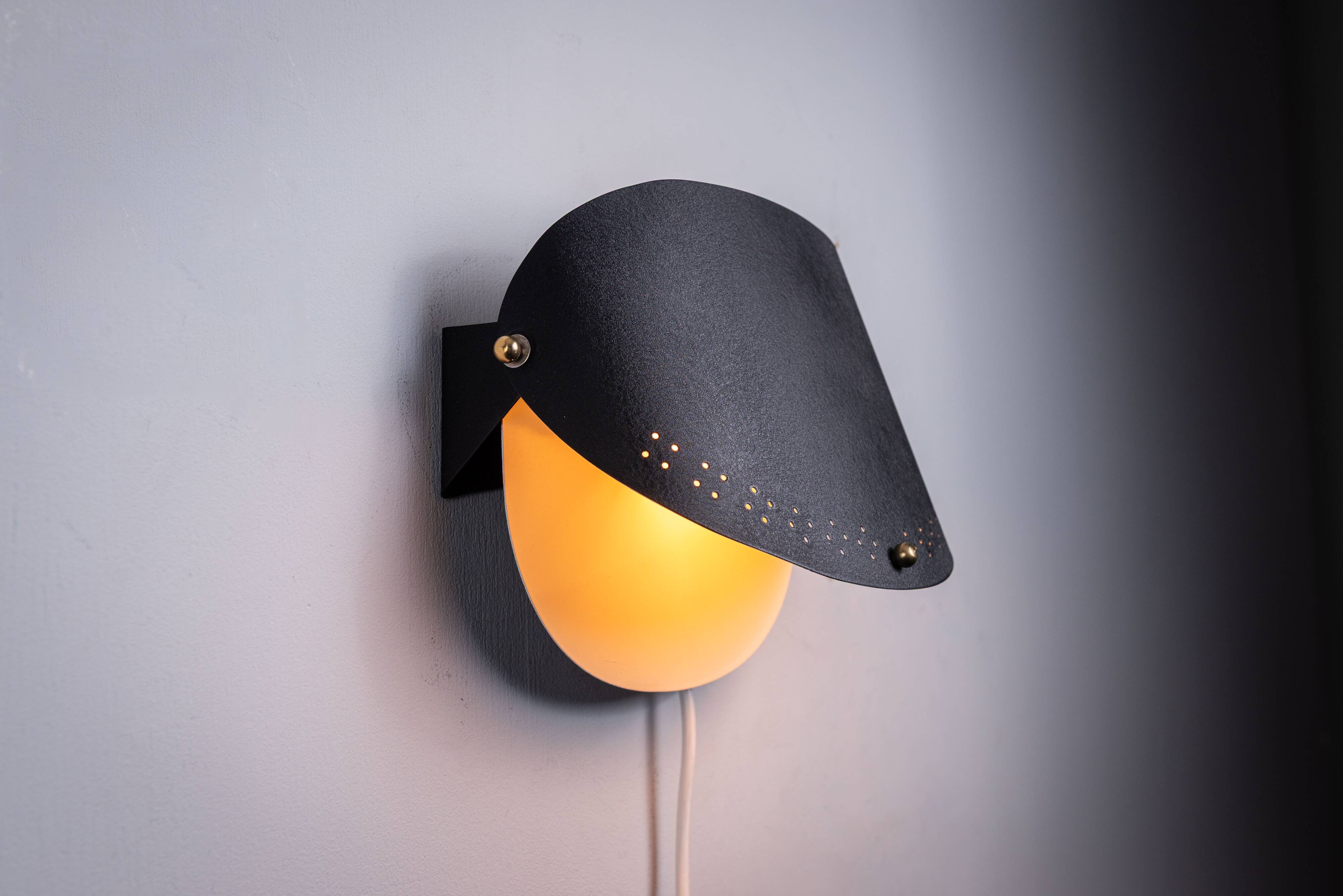 Matte black wall lamps with perforated shades and brass details