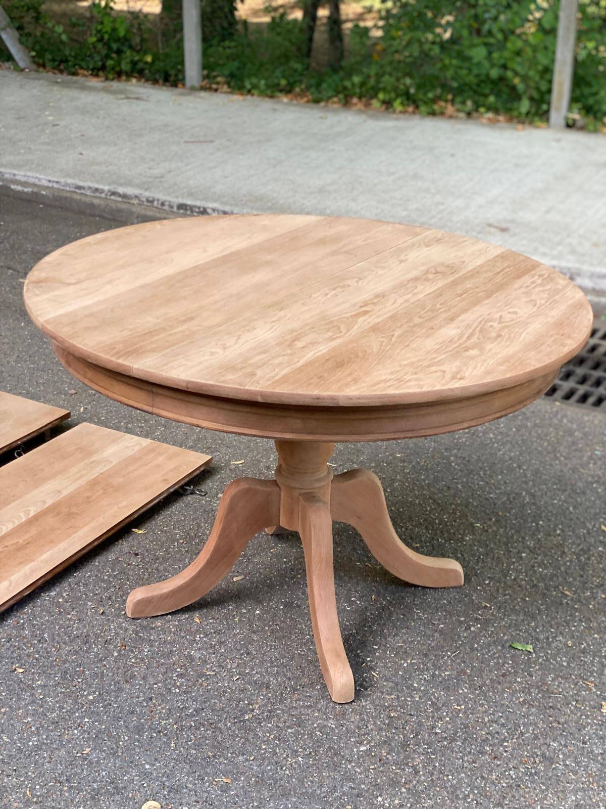 Large extendable round dining table stripped in solid cherry wood with a central leg.