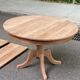 Large extendable round dining table stripped in solid cherry wood with a central leg.