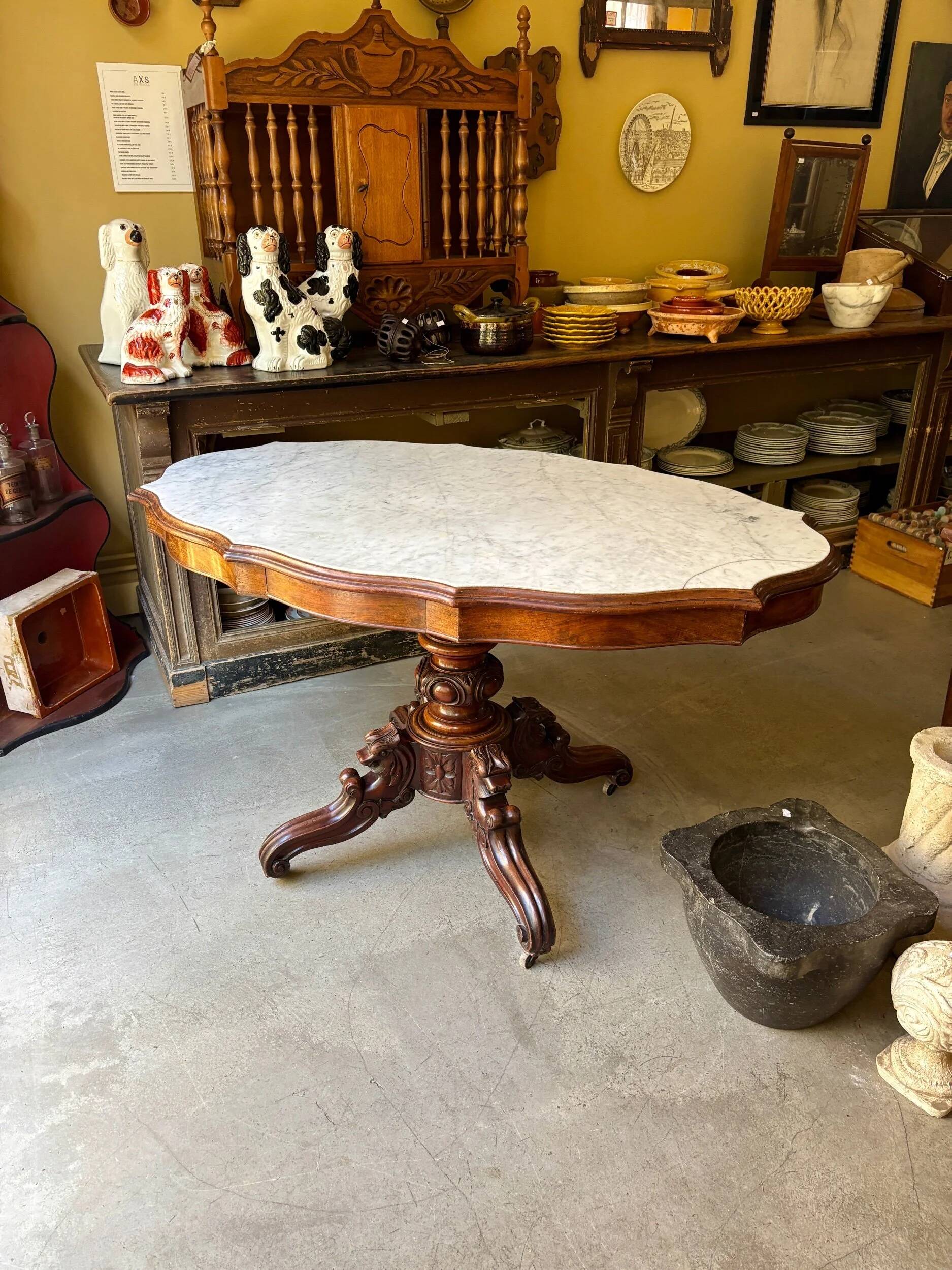 Table with a carved wooden frame and grey marble top on wheels, measuring 130 x 82 cm.