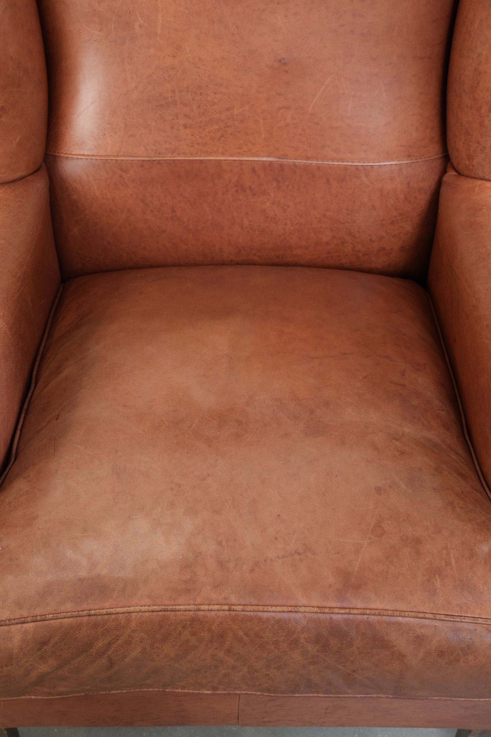Fauteuil anglais à oreilles de couleur cognac clair en cuir de vache.