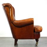 Subtle sheepskin wing chair in good condition on brass front wheels