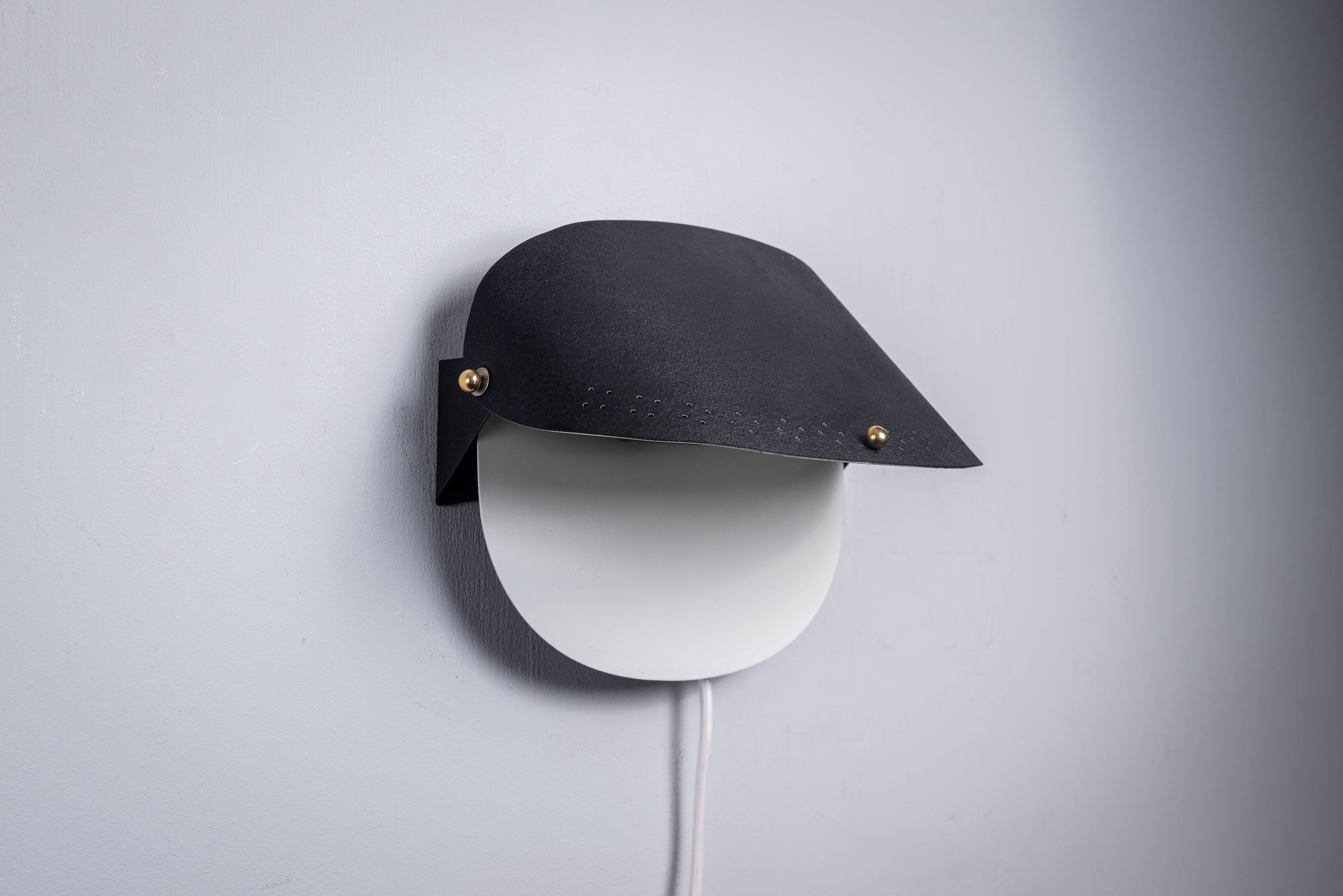 Matte black wall lamps with perforated shades and brass details