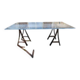 Vintage table with a glass top and smoked plastic trestle legs.