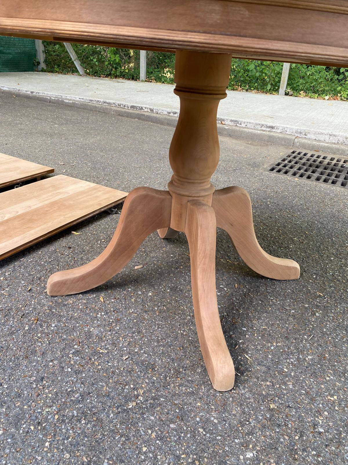 Large extendable round dining table stripped in solid cherry wood with a central leg.