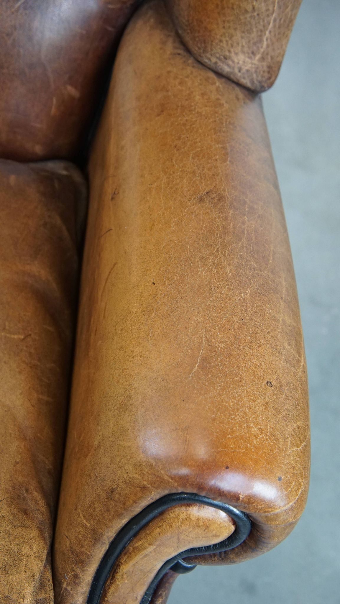 Cognac-colored sheep leather wingback chair finished with black piping