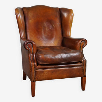 Very rugged wingback armchair made of cognac-colored sheep leather finished with decorative nail hea