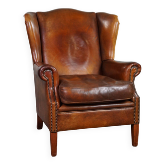 Fauteuil à oreilles très robuste en cuir de mouton de couleur cognac fini avec des clous décoratifs