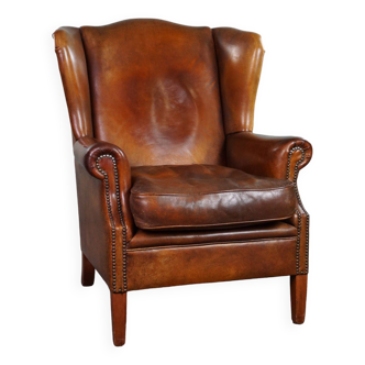 Very rugged wingback armchair made of cognac-colored sheep leather finished with decorative nail hea