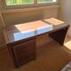 Large wooden desk with a glass top and a wheeled drawer unit.