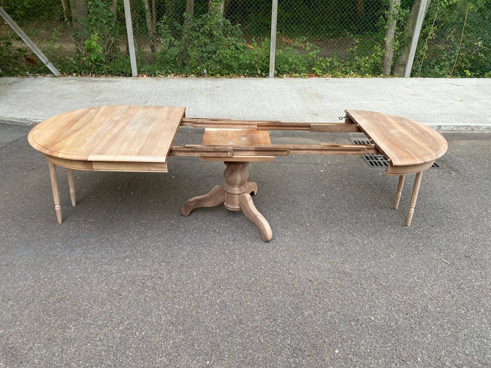 Round extendable dining table stripped in solid raw walnut with a central leg.