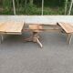 Round extendable dining table stripped in solid raw walnut with a central leg.