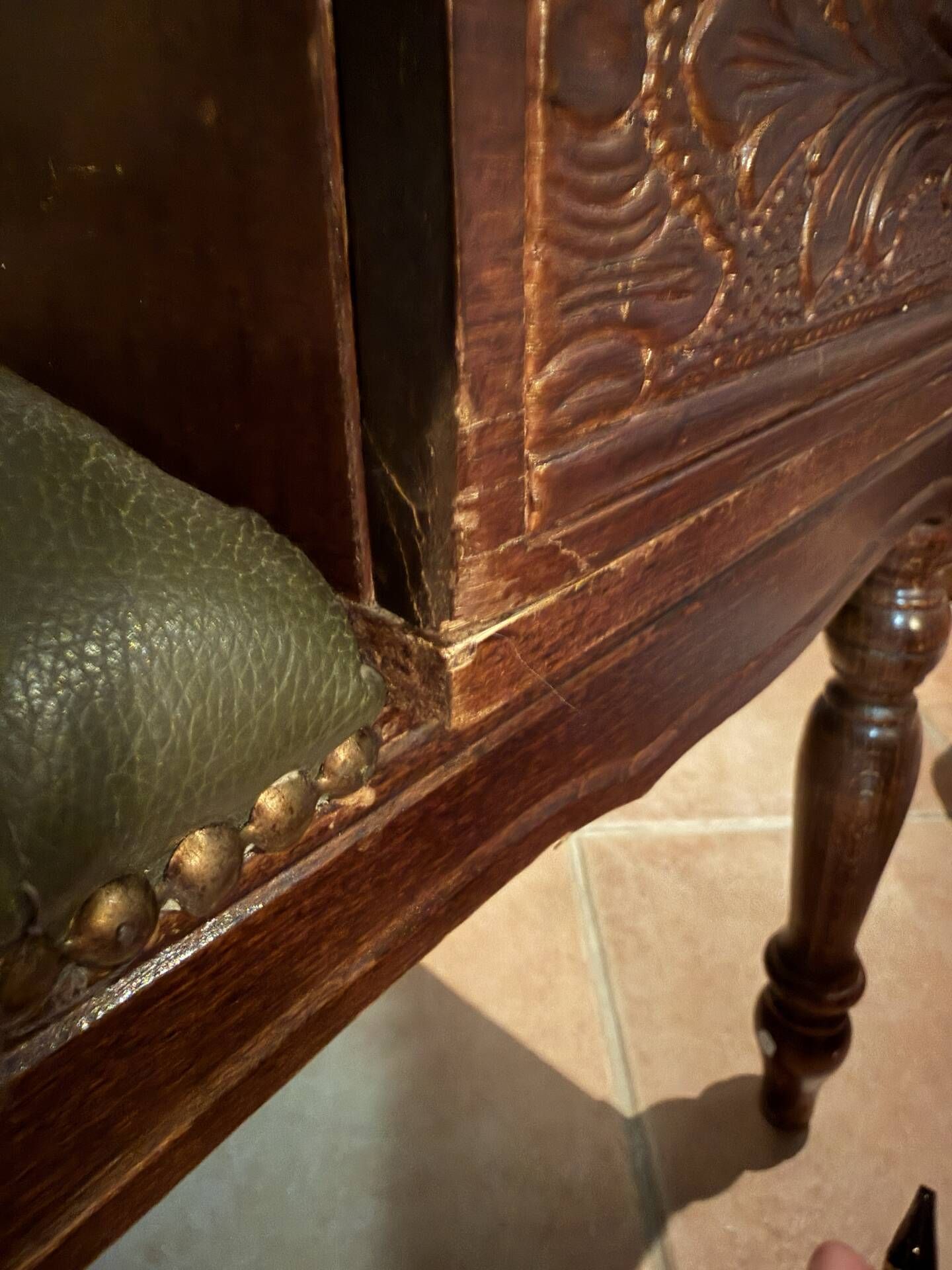 Antique carved wooden bench with green upholstered seat and backrest.