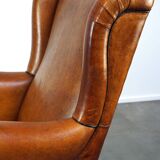 Subtle sheepskin wing chair in good condition on brass front wheels