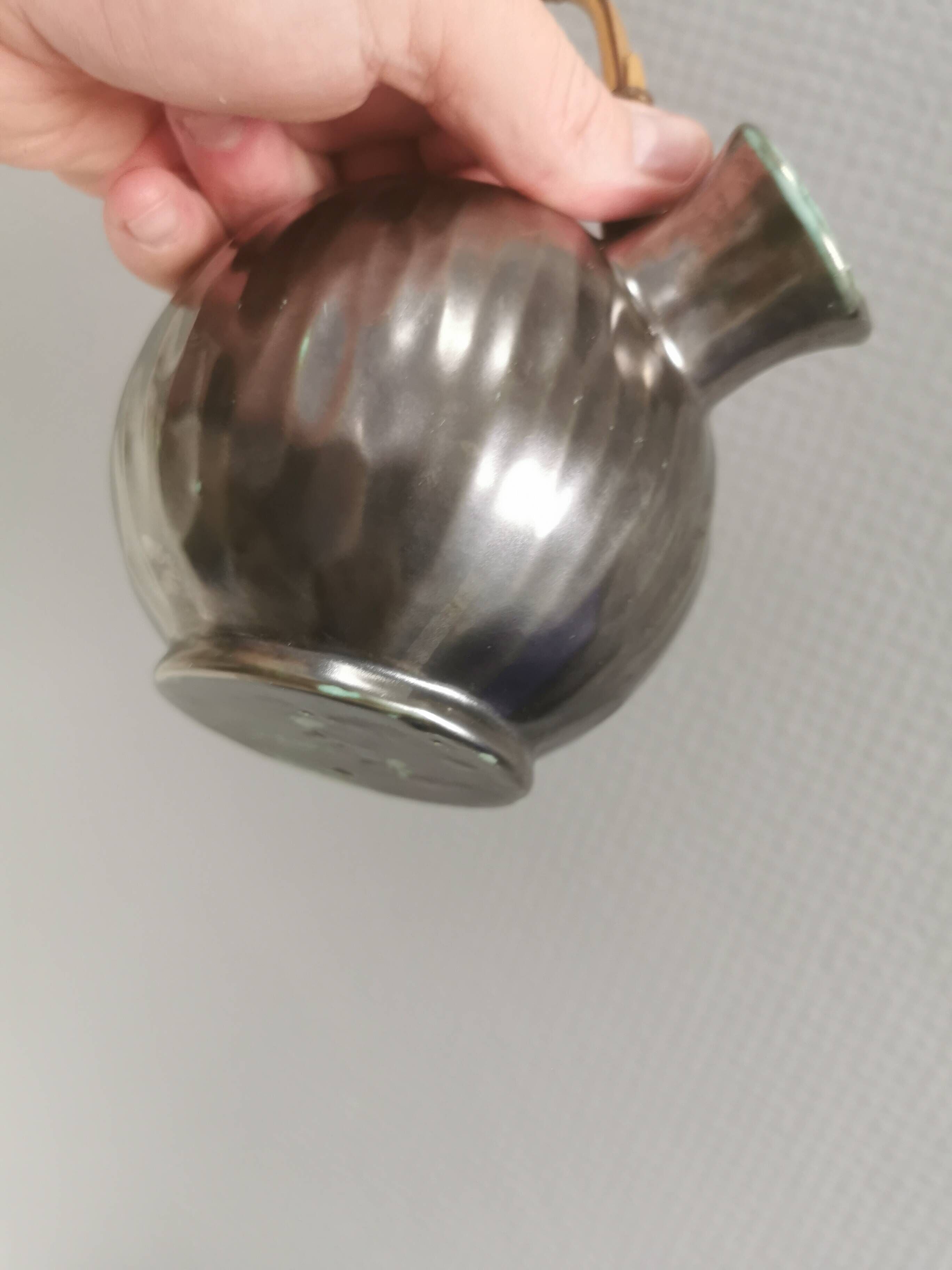 A ceramic jug with a metallic glaze and a handle made of woven raffia.