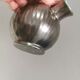 A ceramic jug with a metallic glaze and a handle made of woven raffia.
