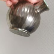 A ceramic jug with a metallic glaze and a handle made of woven raffia.