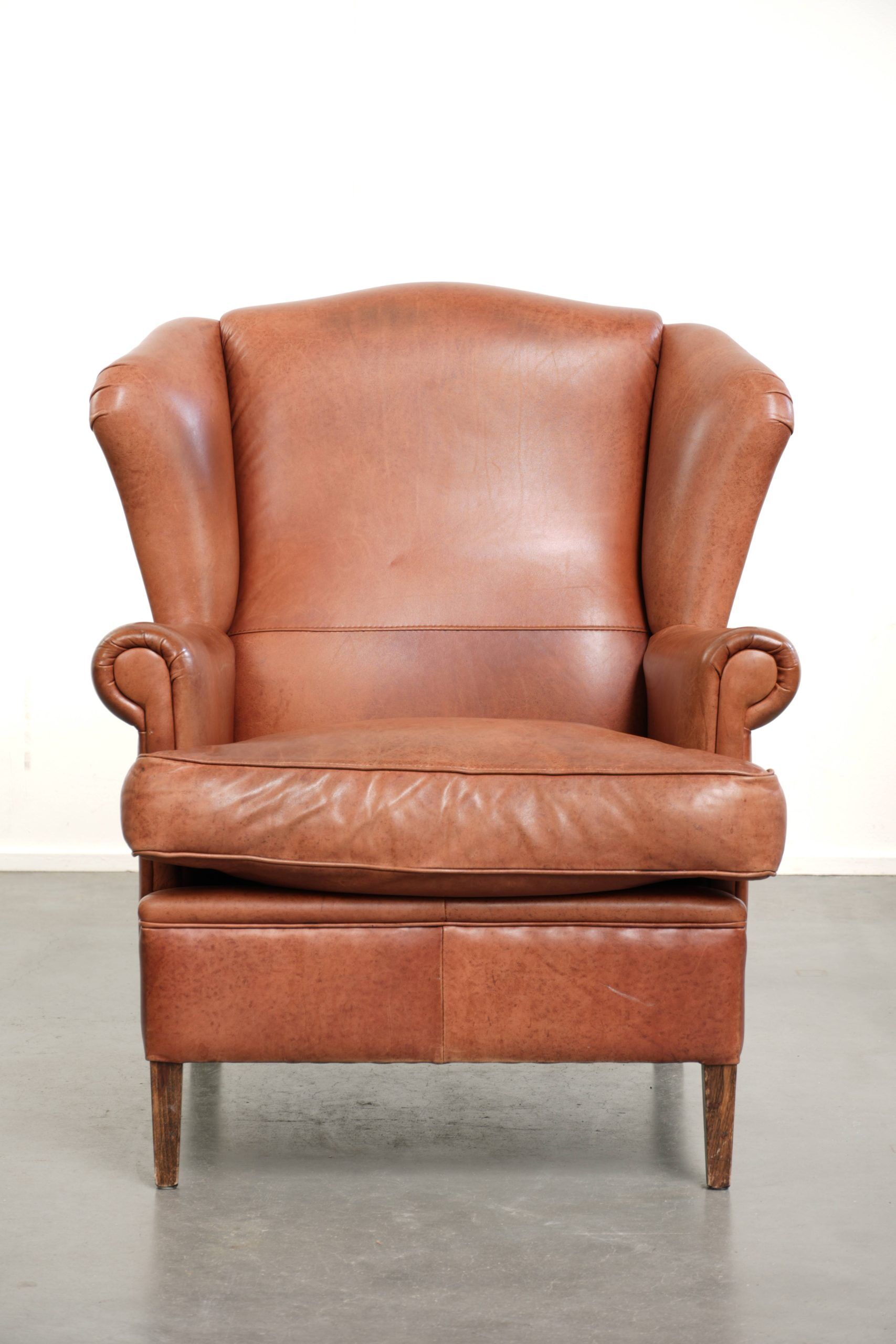 Light cognac-coloured cow leather wingback armchair with matching piping