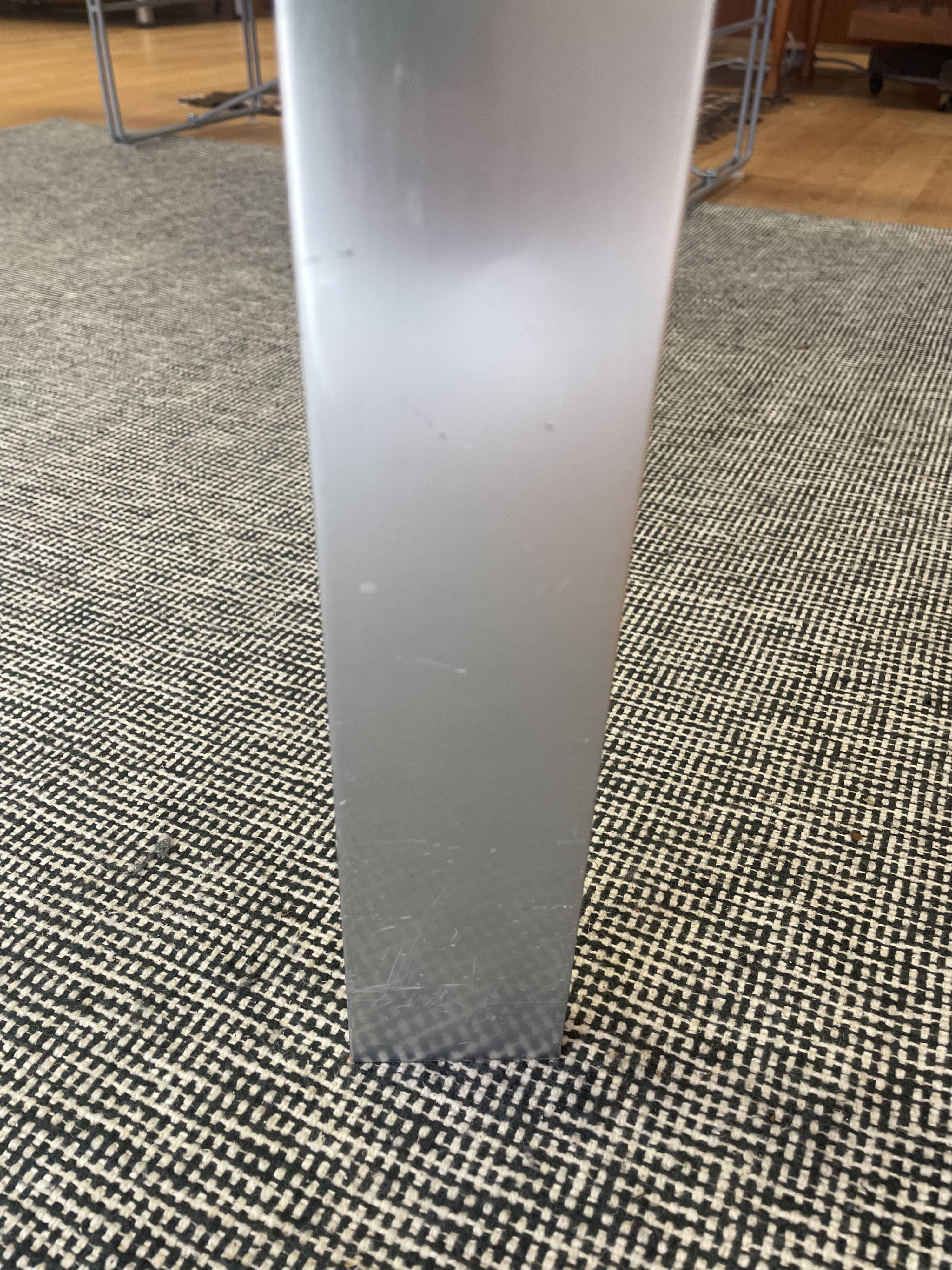 Round dining table with a glass top and brushed metal triangular frame.