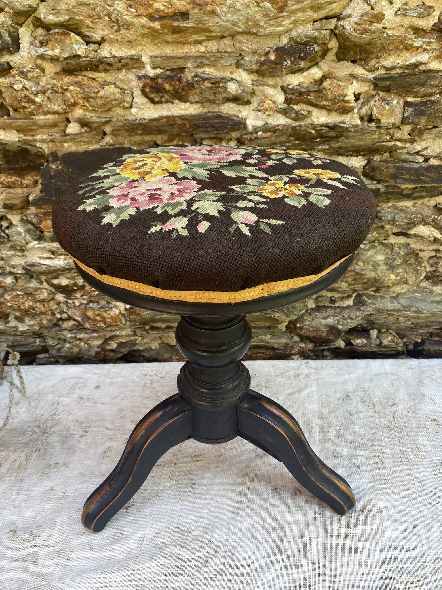 Old adjustable piano stool, blackened wood, metal screws, embroidered seat.