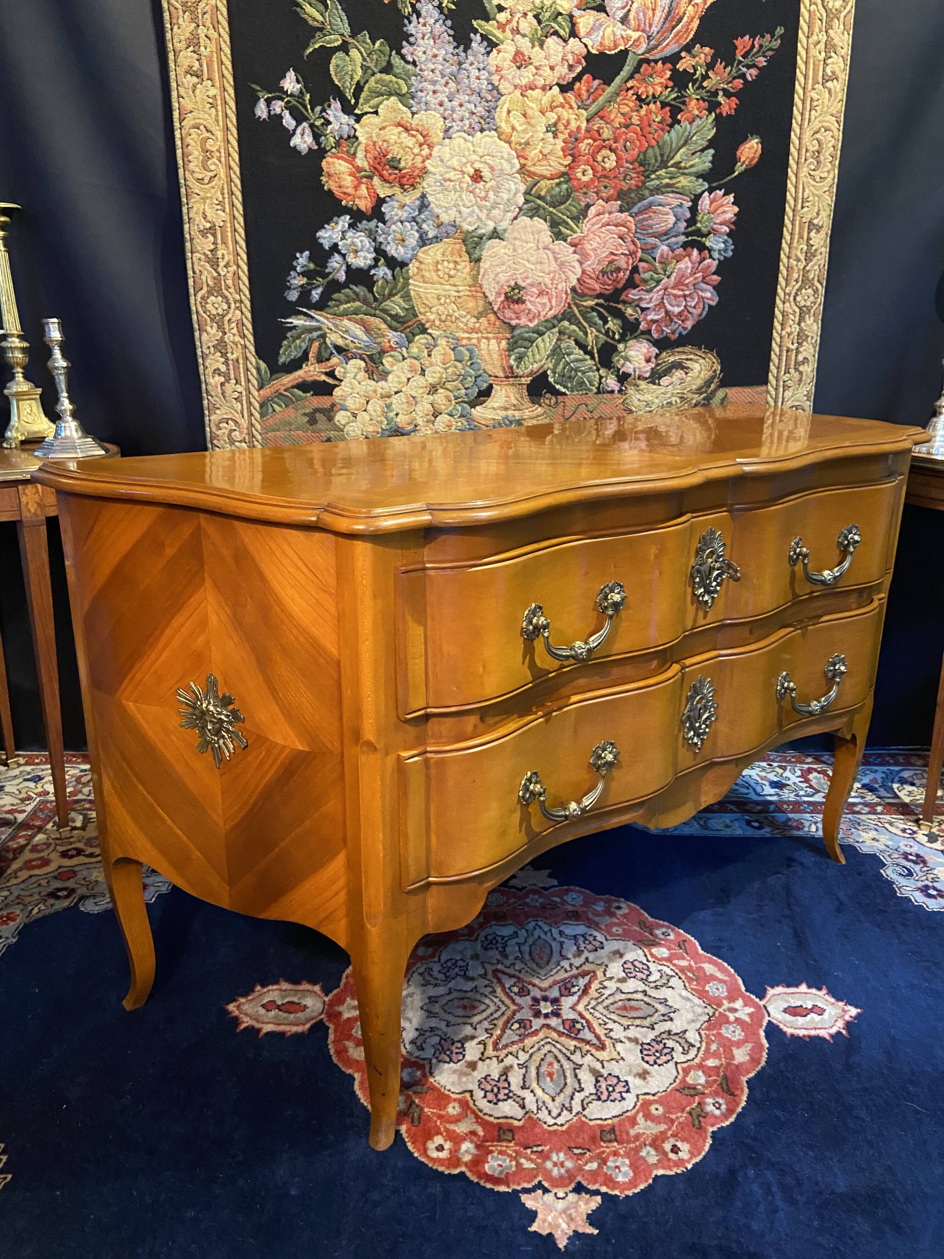 Large bow-fronted chest of drawers in blonde cherry with bronze ornamentation.