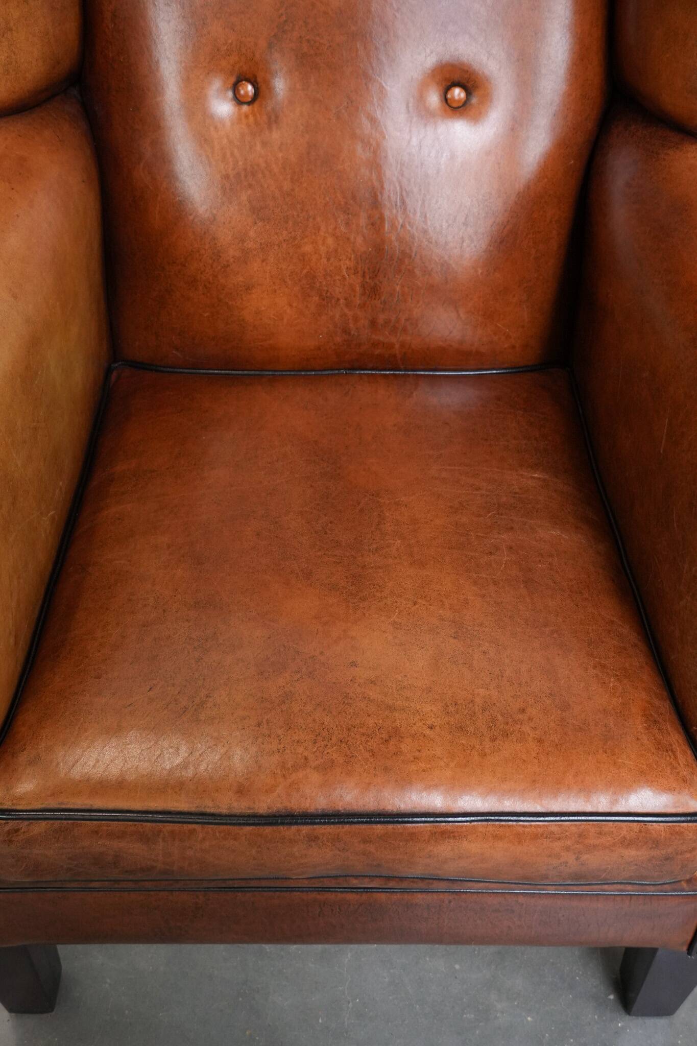 Large sheepskin wingback chair with black piping and decorative nails