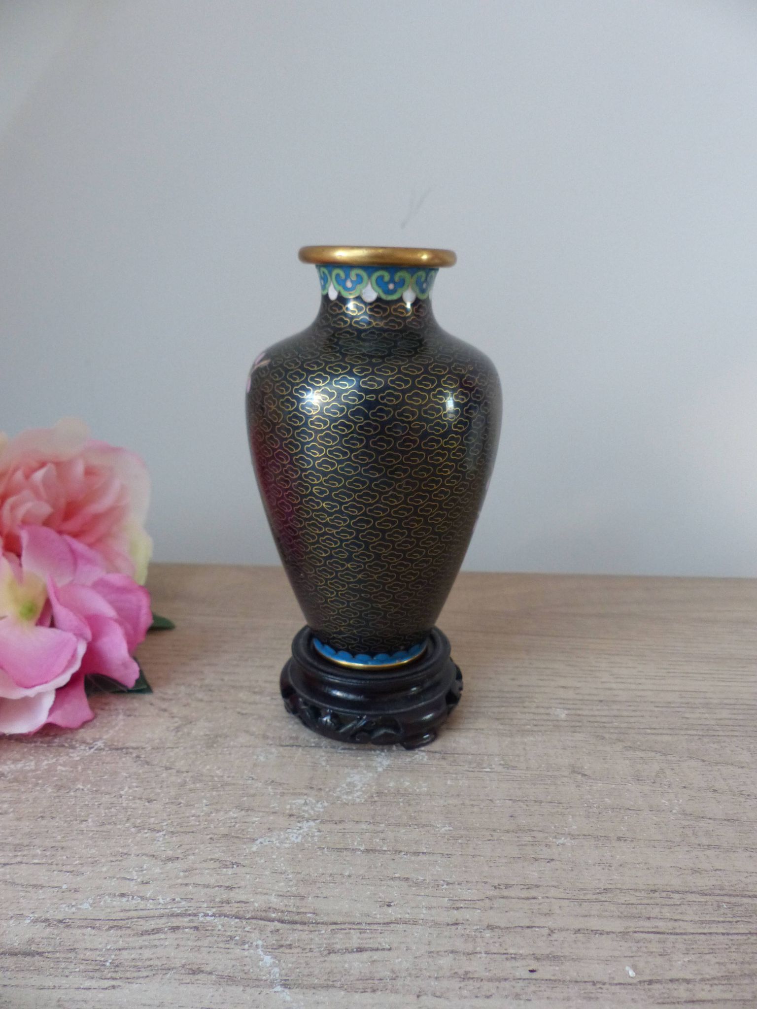 Small black cloisonné vase decorated with yellow and pink cherry blossoms, vase on wooden base