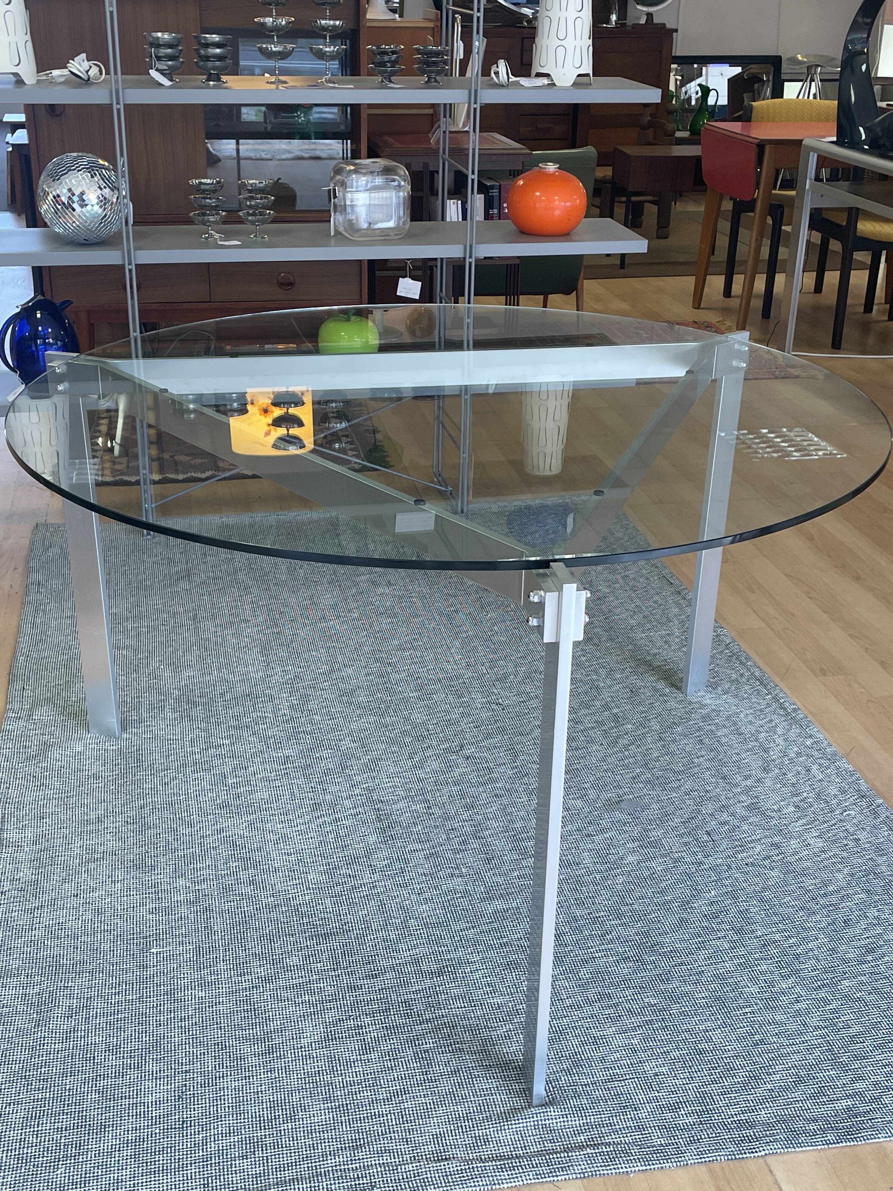Round dining table with a glass top and brushed metal triangular frame.