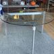 Round dining table with a glass top and brushed metal triangular frame.