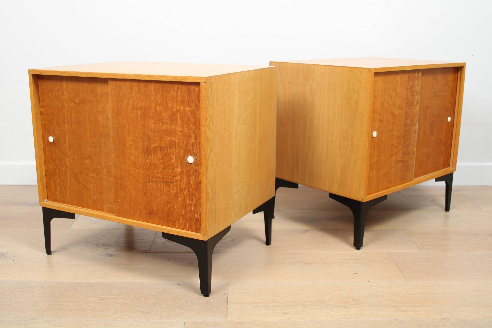 A pair of vintage mid-century bedside tables with oak sliding doors