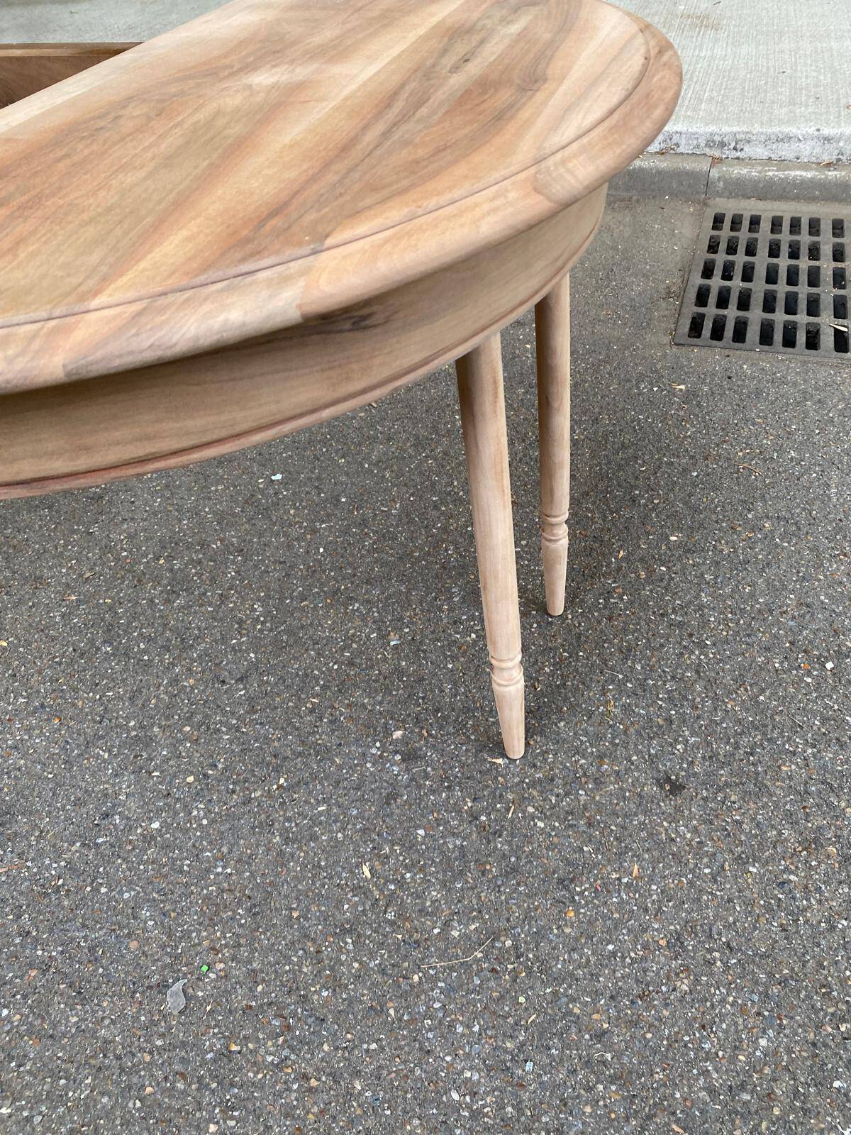 Round extendable dining table stripped in solid raw walnut with a central leg.