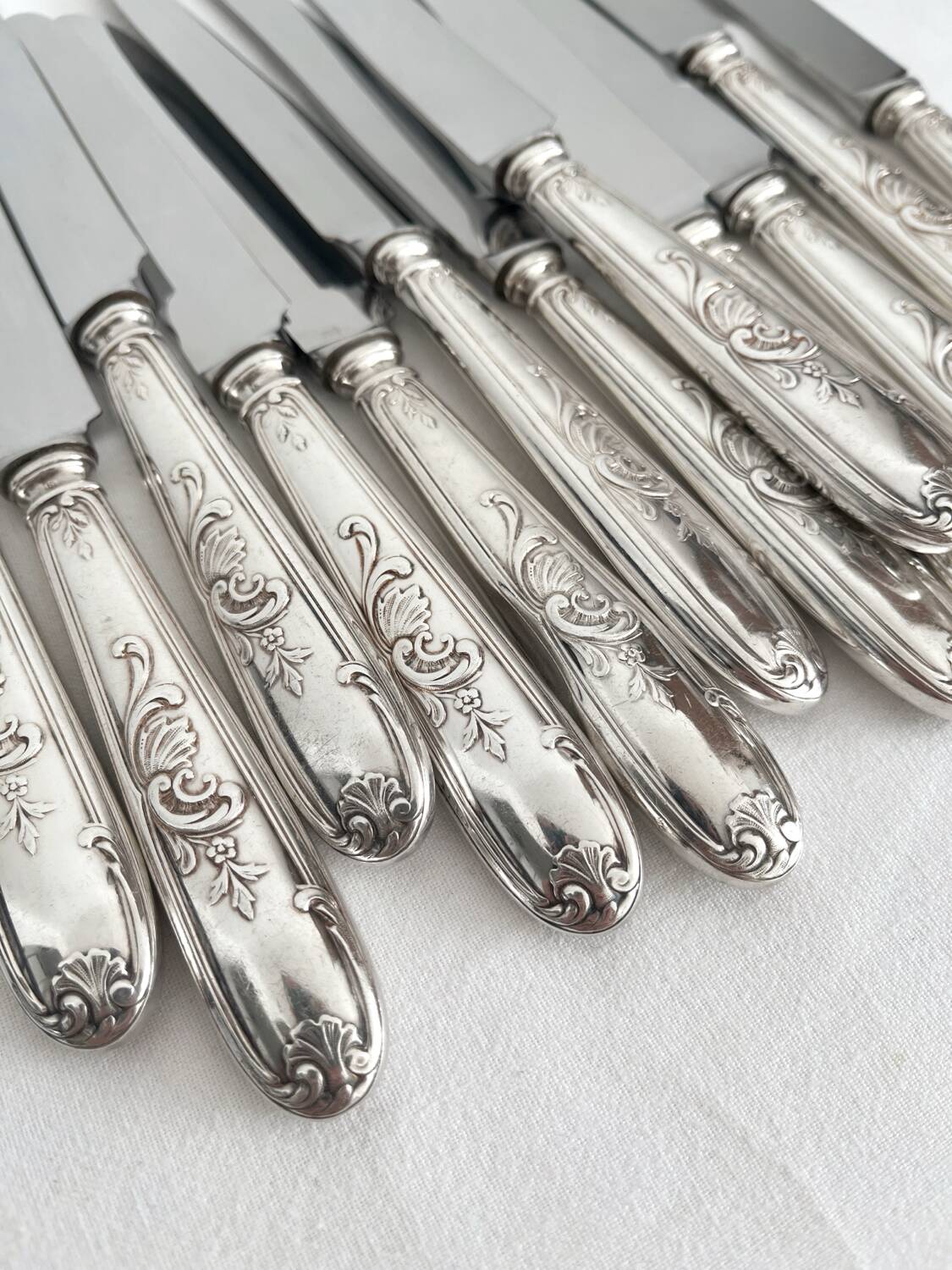 12 antique silver-plated knives with acanthus shell decoration and stainless steel blades.