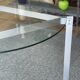 Round dining table with a glass top and brushed metal triangular frame.