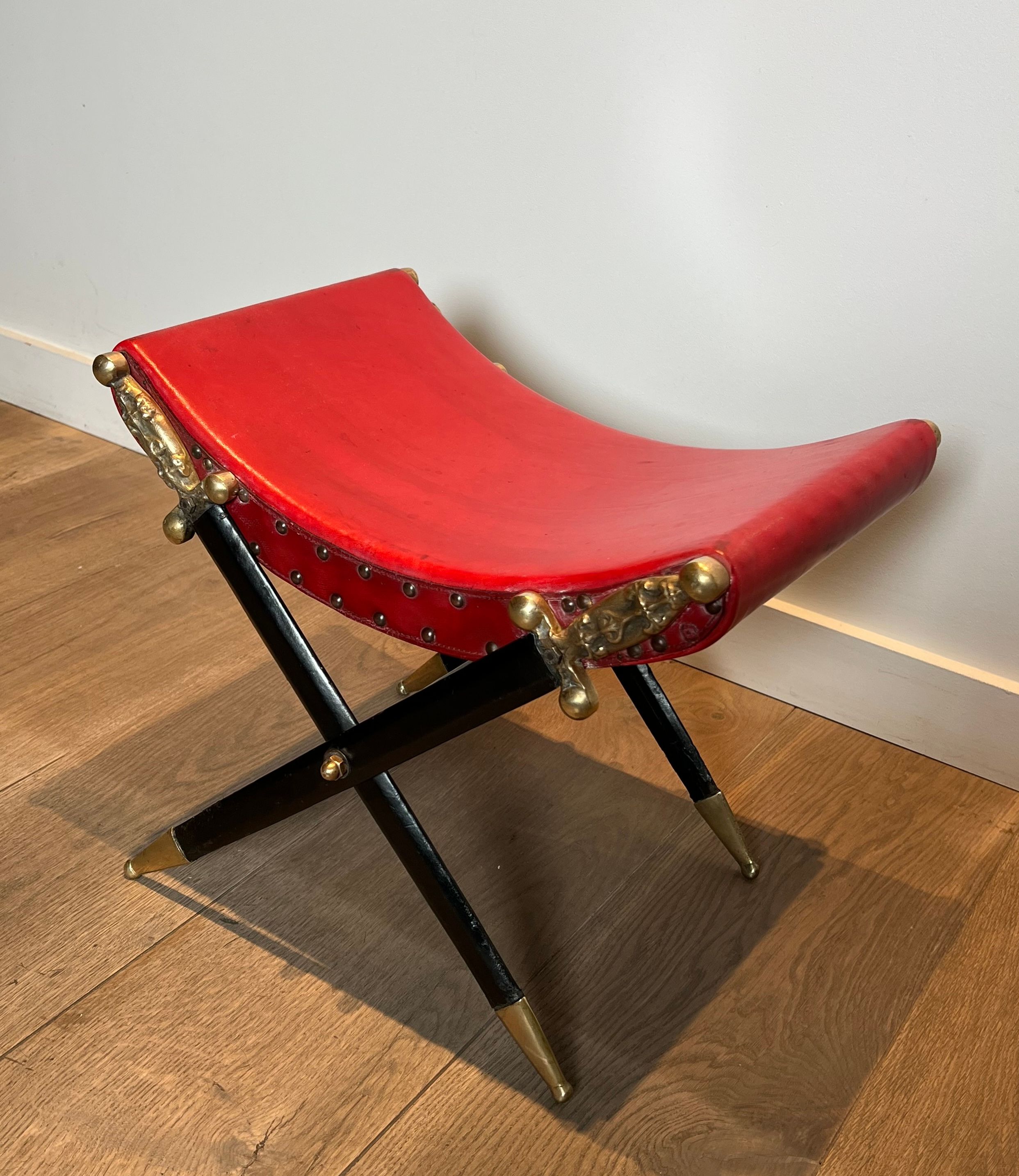 Neoclassical curule stool in red leather, decorated with crossed swords in bronze and metal covered in black leather.