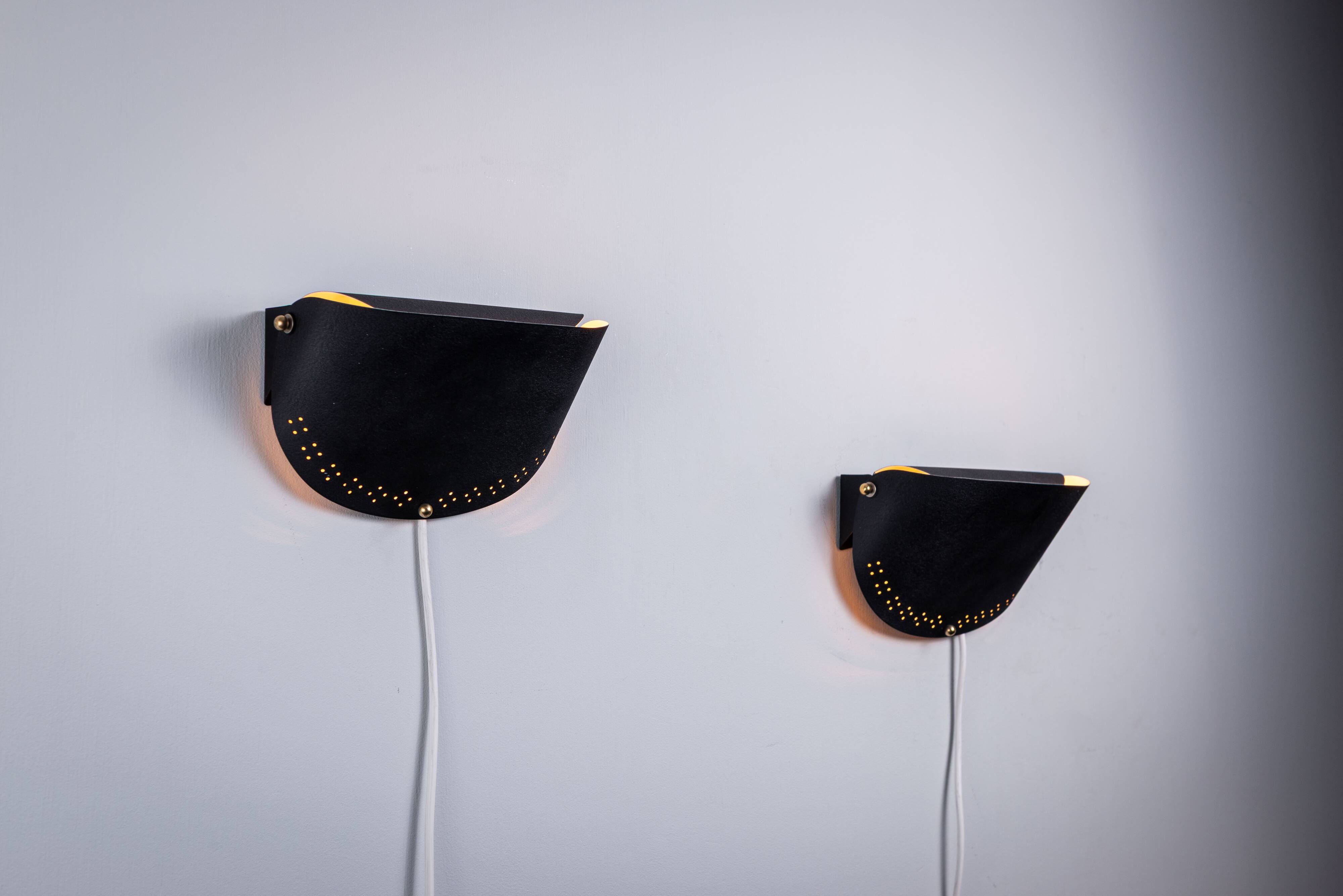 Matte black wall lamps with perforated shades and brass details