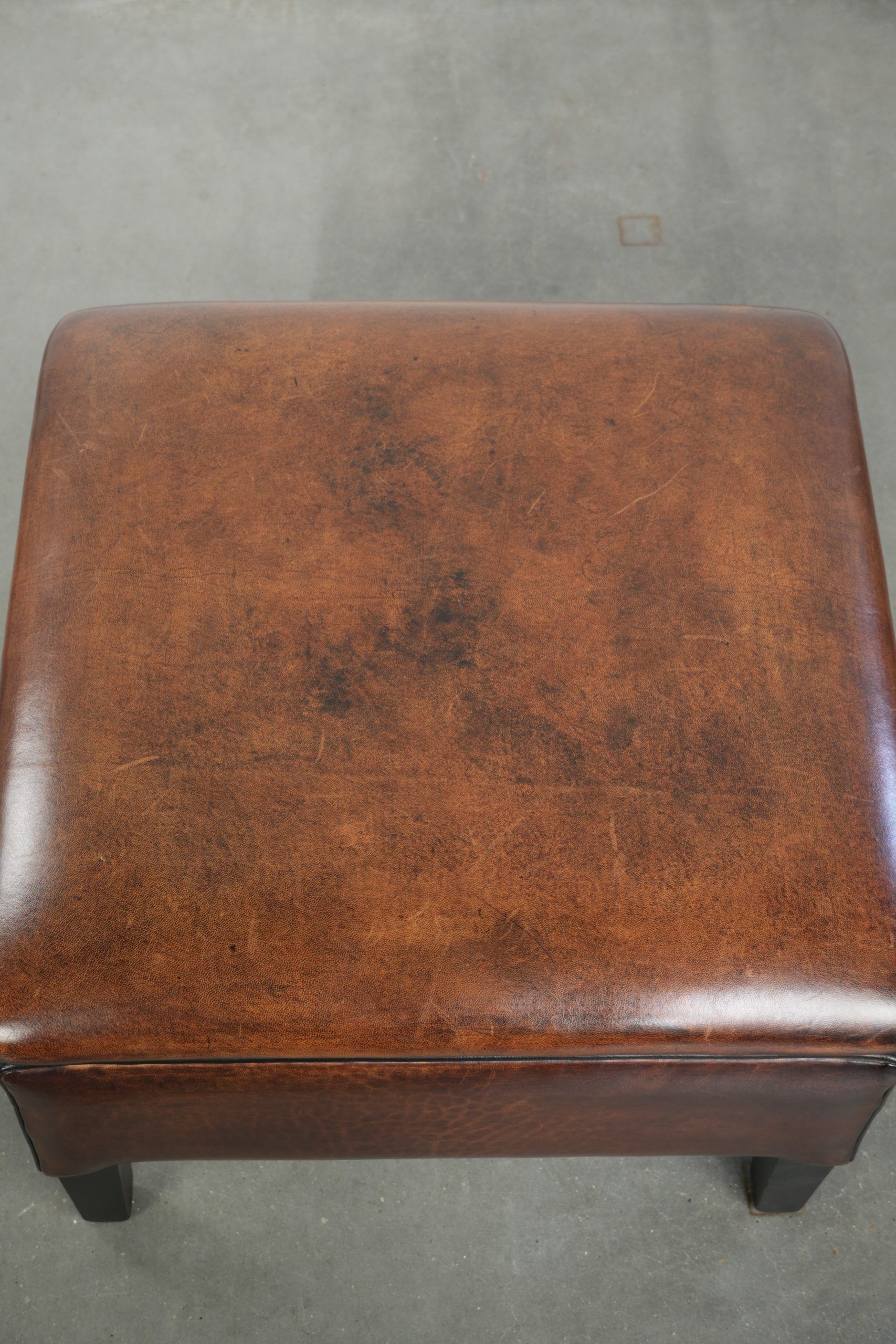 Large dark brown square ottoman made of sheepskin with black piping