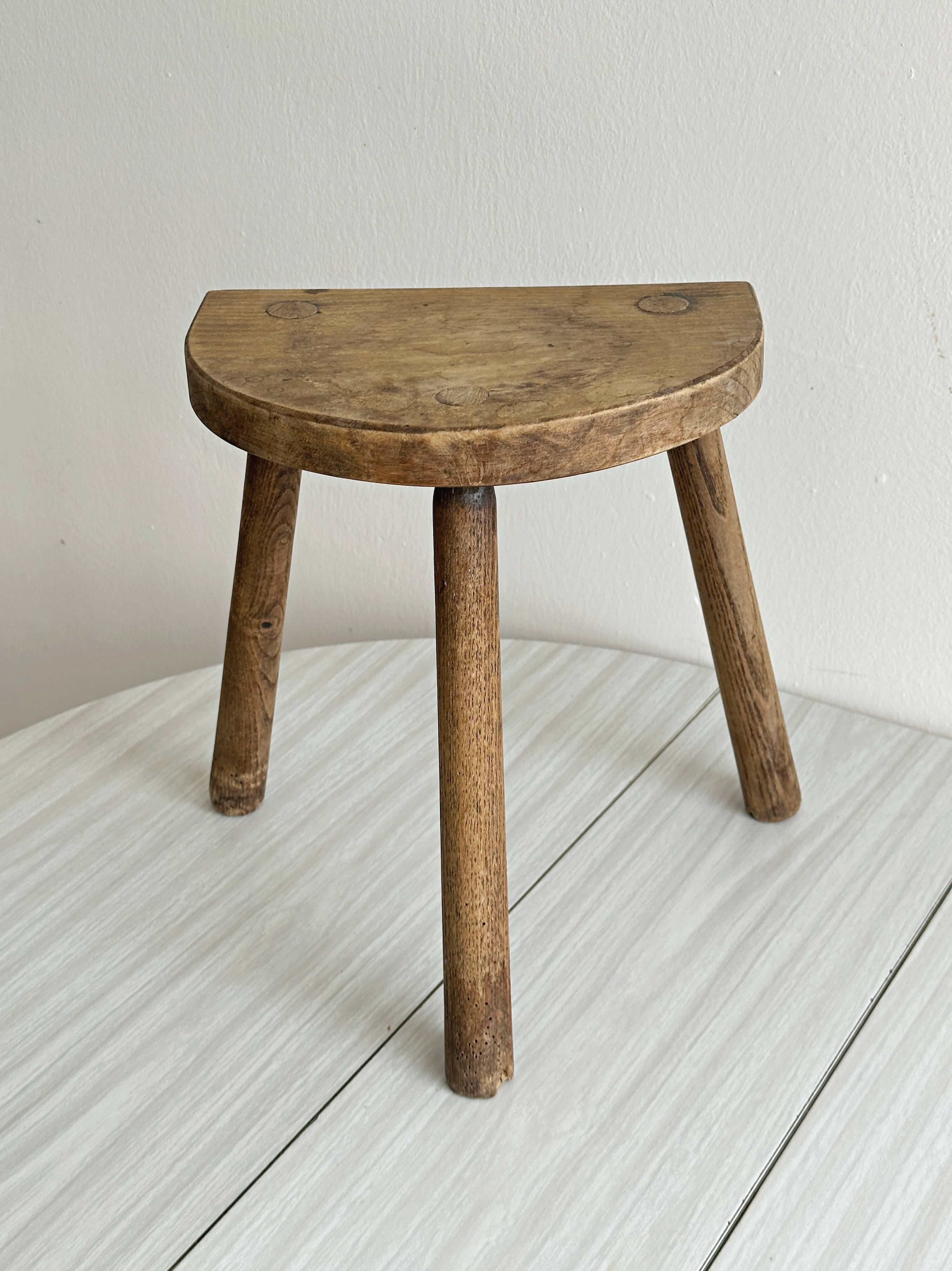 Small antique tripod stool in light wood, half-moon seat.