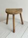 Small antique tripod stool in light wood, half-moon seat.
