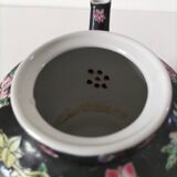 Vintage Chinese teapot with floral polychrome decoration on a black background.