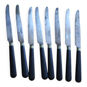A set of 8 knives with black wooden handles and bolsters.