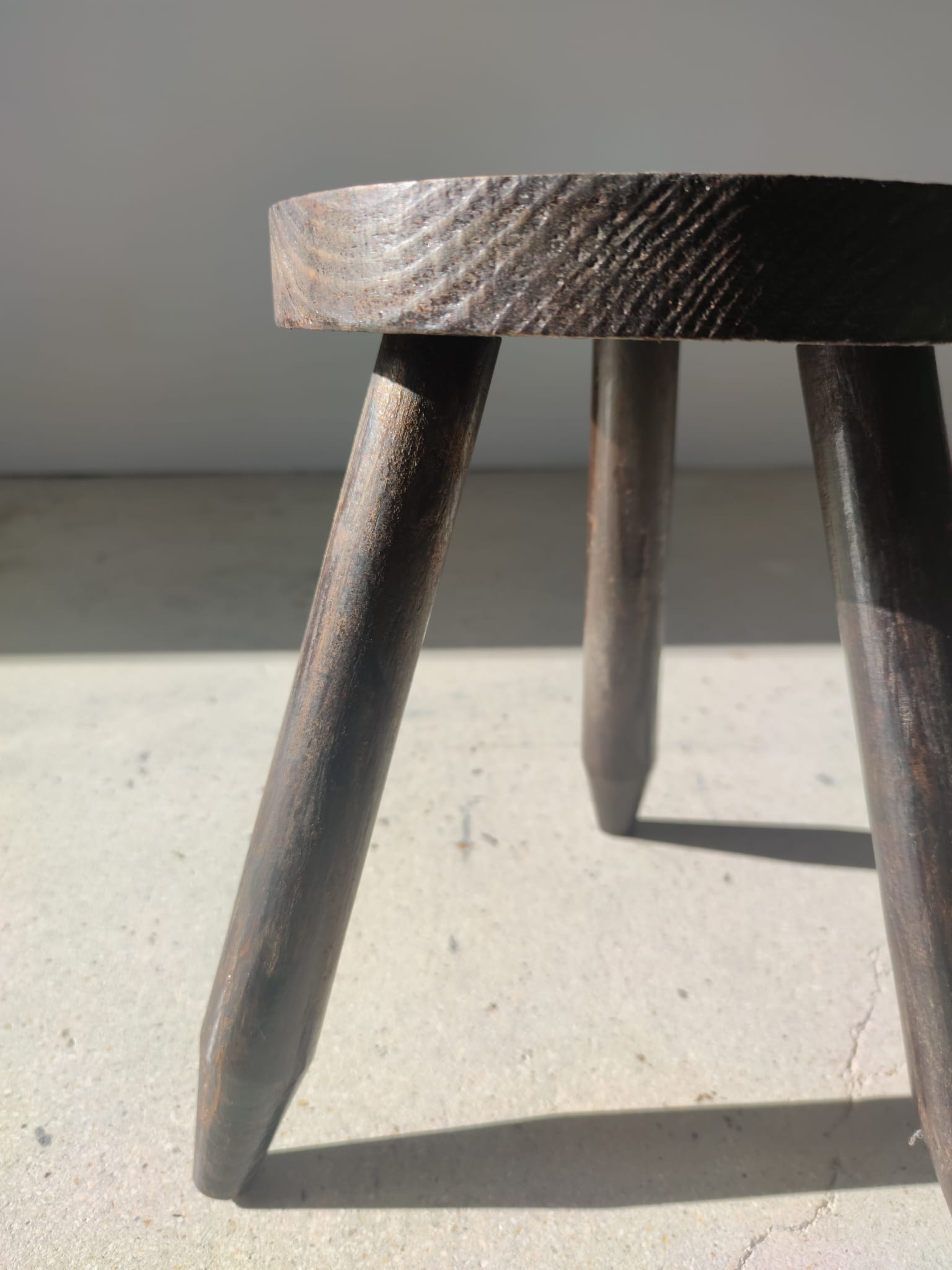 Small brutalistic tripod stool in dark wood tapered feet circular seat