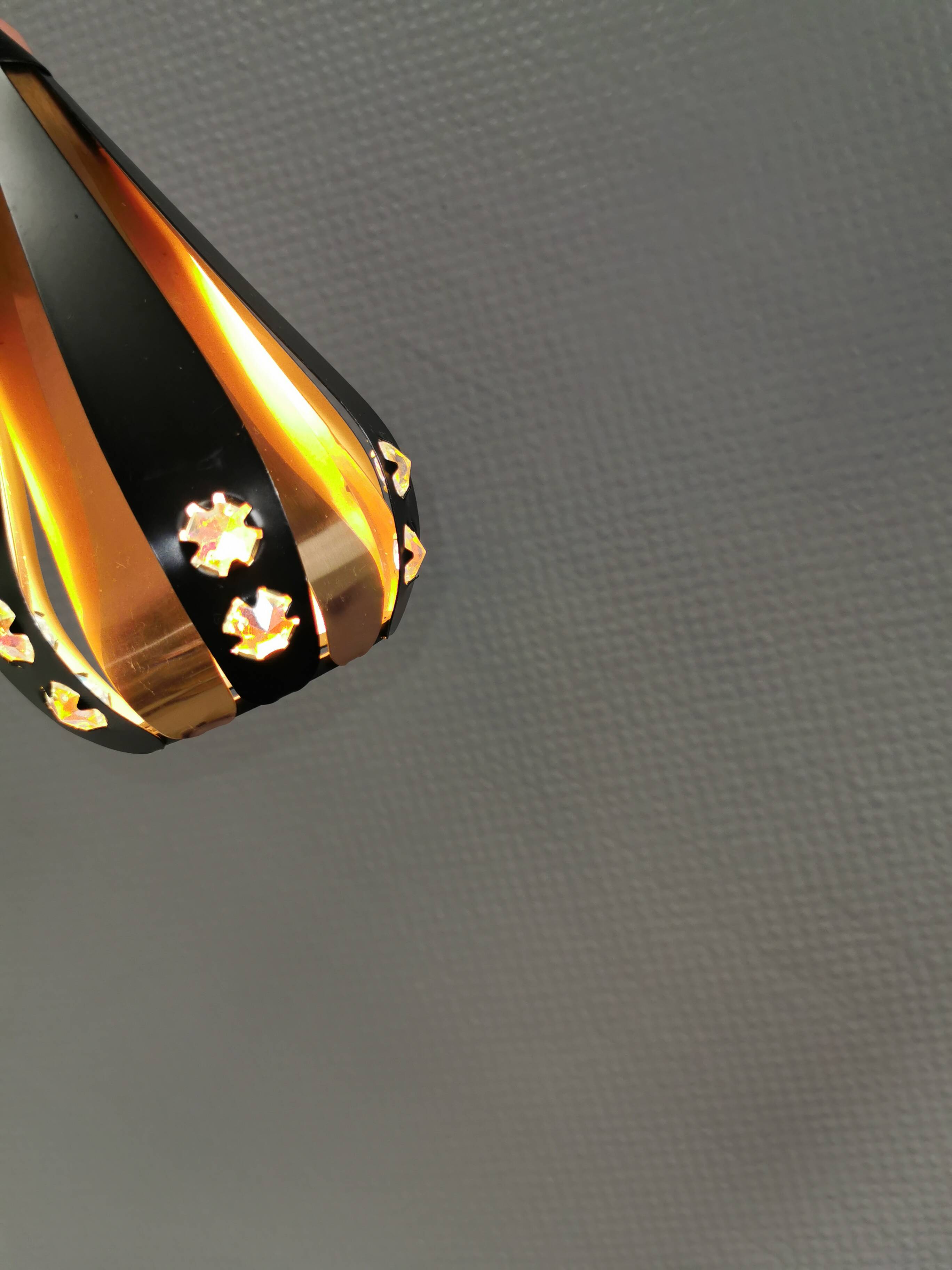 A teardrop-shaped pendant lamp made of copper, black metal, and prisms.