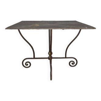 Wrought iron table with a sculptural base, adorned with scrolls.
