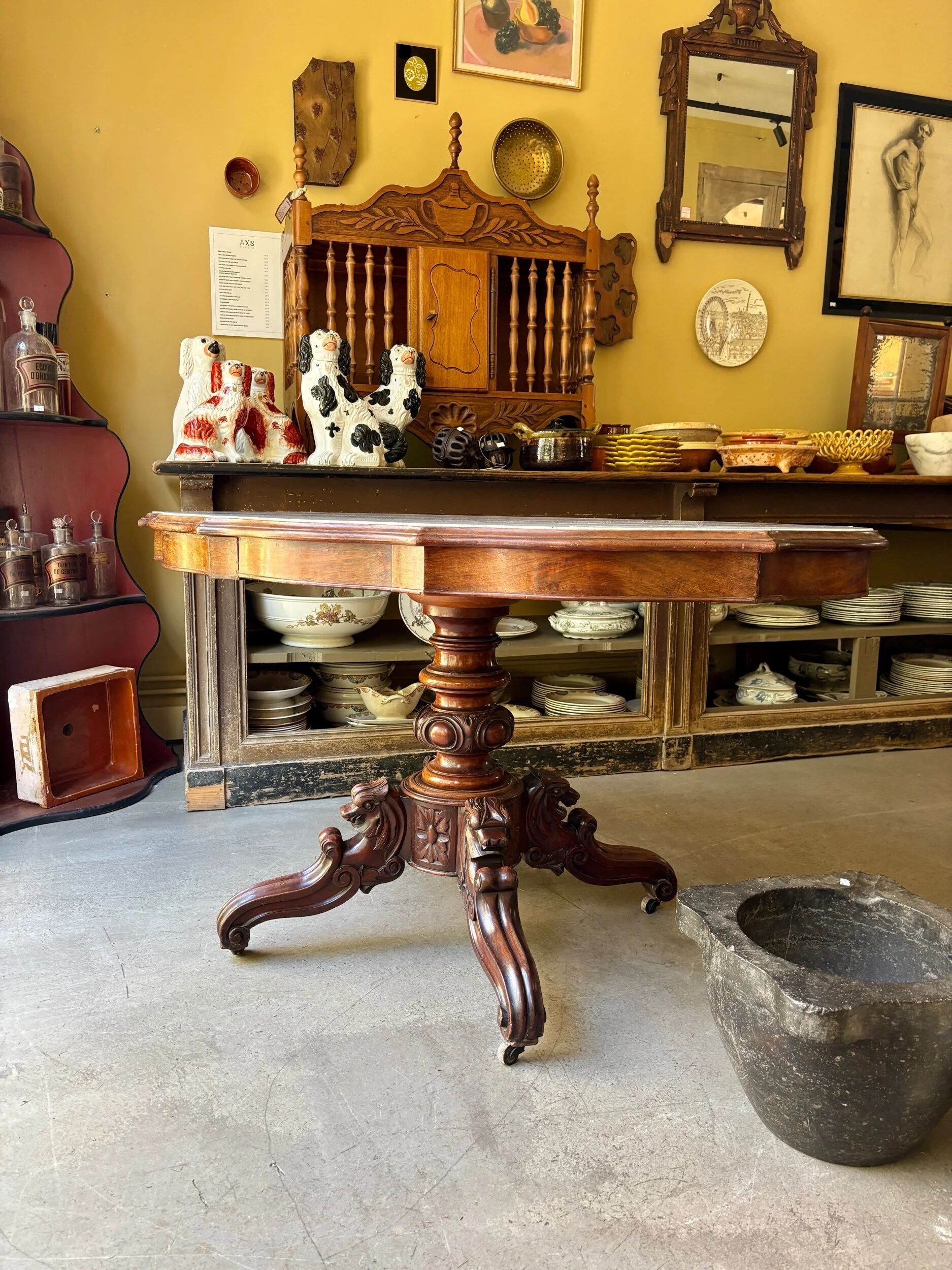 Table with a carved wooden frame and grey marble top on wheels, measuring 130 x 82 cm.