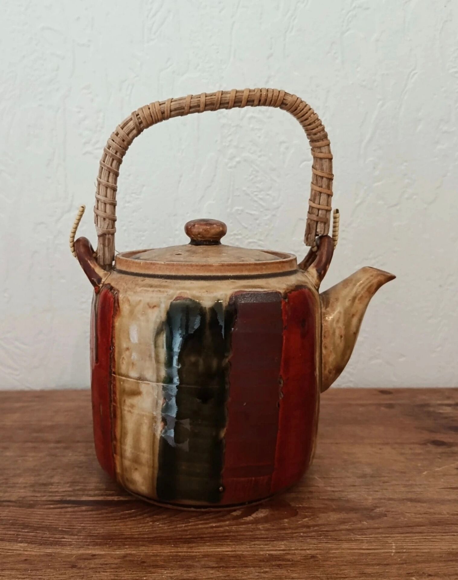 Vintage ceramic teapot with an enamel finish, rattan handle, warm tones.