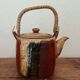 Vintage ceramic teapot with an enamel finish, rattan handle, warm tones.